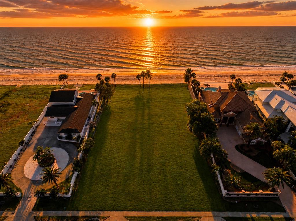 An aerial view shows a vacant beachfront lot situated between two residential properties and a road — 1420 and 1440 GULF BOULEVARD, BELLEAIR SHORE, FL