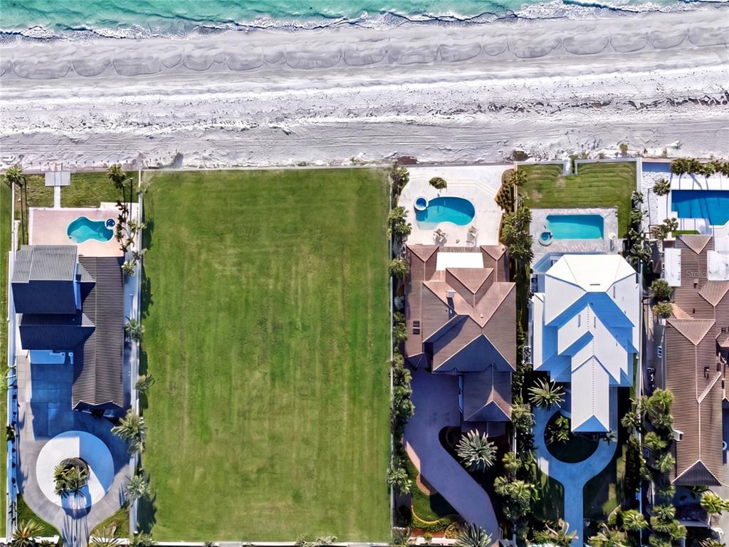 An aerial view shows a vacant, rectangular grassy lot situated between two large beachfront houses — 1420 and 1440 GULF BOULEVARD, BELLEAIR SHORE, FL