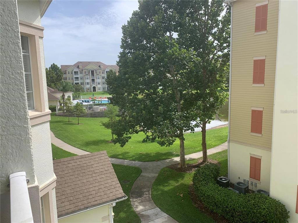 An elevated view shows a grassy courtyard with a walkway, trees, and a swimming pool — 5255 CANE ISLAND LOOP UNIT 304, KISSIMMEE, FL
