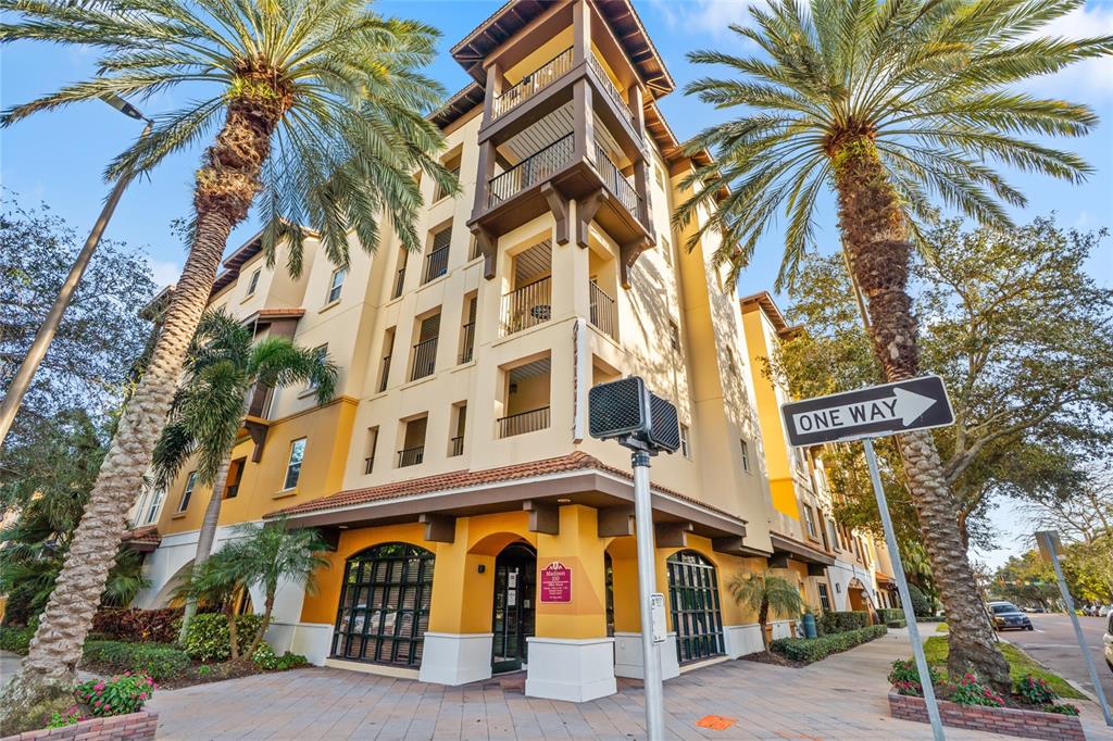 A multi-story yellow apartment building with balconies stands next to palm trees and a street — 100 4TH AVENUE S UNIT 115, ST PETERSBURG, FL