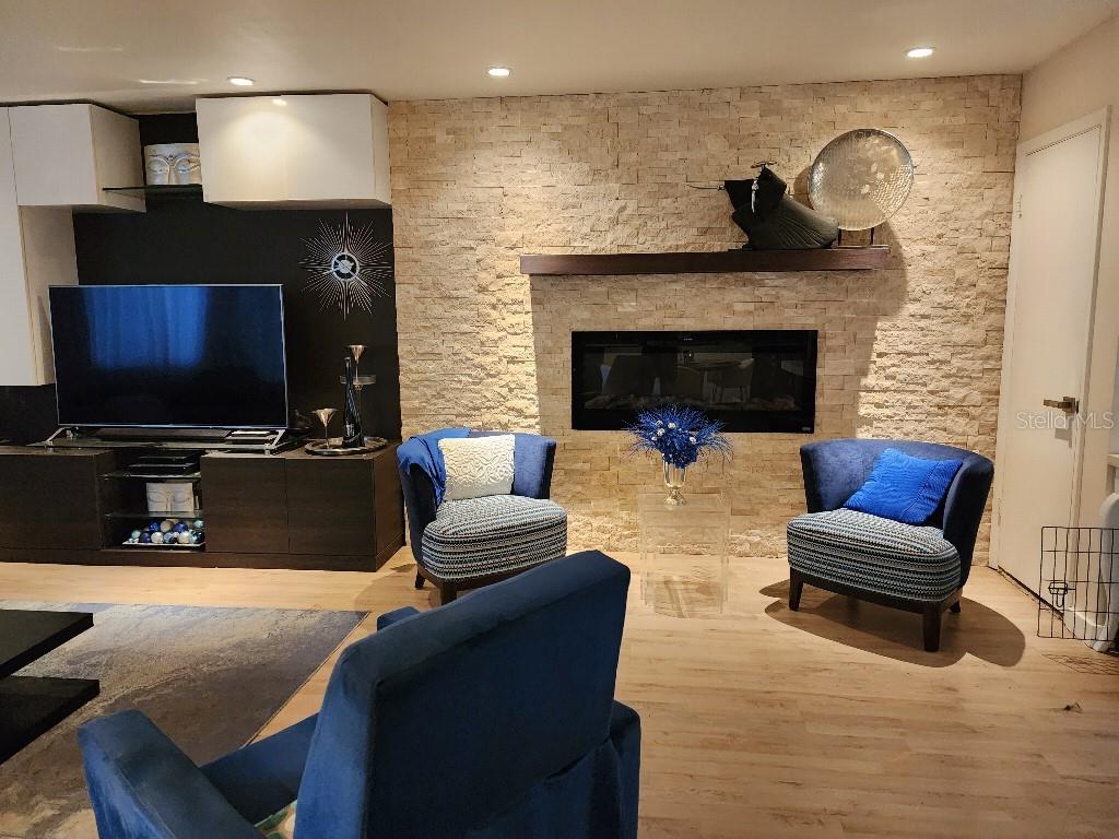 A living room features a stone fireplace, a wall-mounted television, and blue accent chairs — 610 CHESTNUT OAK CIRCLE UNIT 110, ALTAMONTE SPRINGS, FL