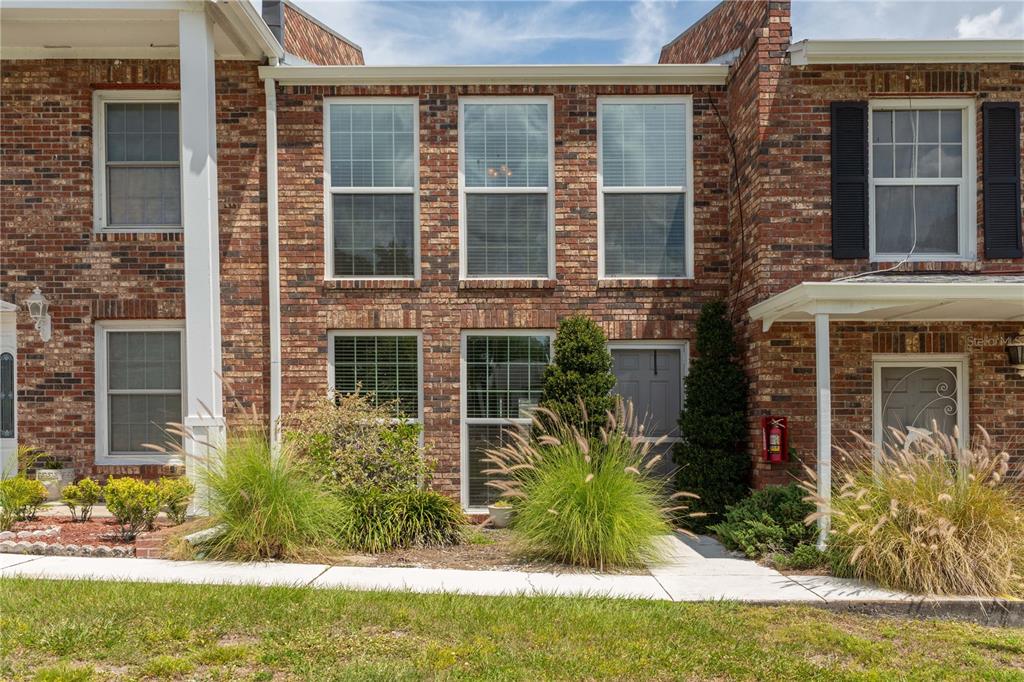 A two-story brick townhouse exterior features multiple windows, a grey front door, and landscaping — 5850 CYPRESS GARDENS BOULEVARD UNIT 607, WINTER HAVEN, FL