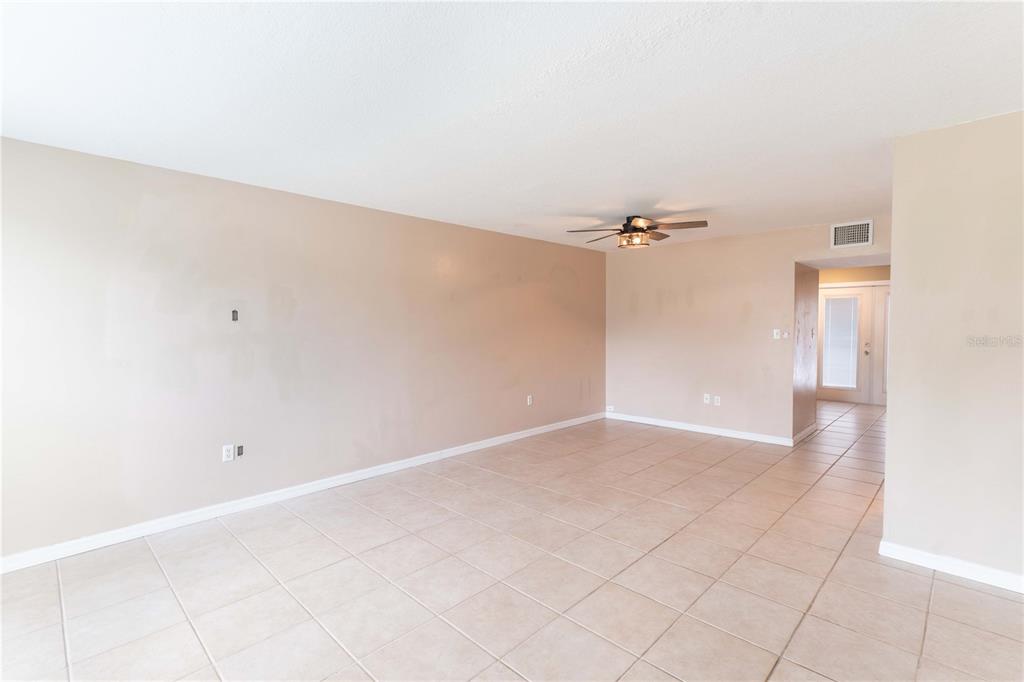 An empty living room features beige walls, a ceiling fan, and light-colored tile flooring — 5850 CYPRESS GARDENS BOULEVARD UNIT 607, WINTER HAVEN, FL