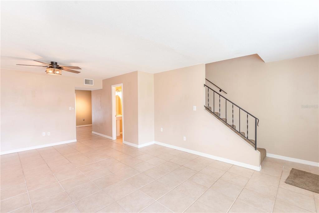 An empty room with beige tile flooring, a ceiling fan, and a staircase with railing — 5850 CYPRESS GARDENS BOULEVARD UNIT 607, WINTER HAVEN, FL