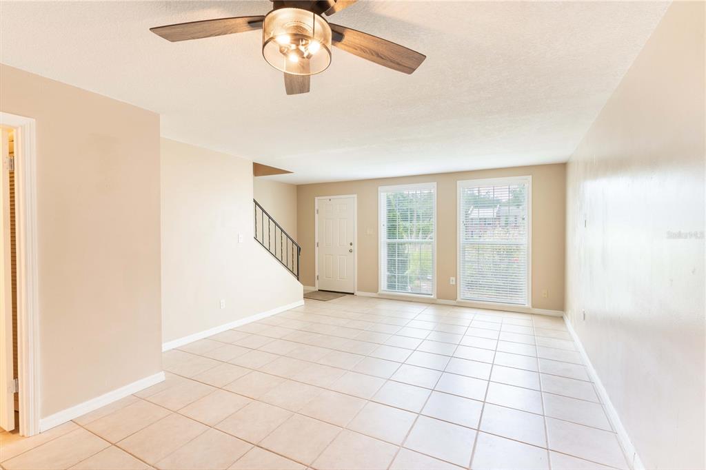A living room with beige walls, tile flooring, a ceiling fan, and a staircase — 5850 CYPRESS GARDENS BOULEVARD UNIT 607, WINTER HAVEN, FL