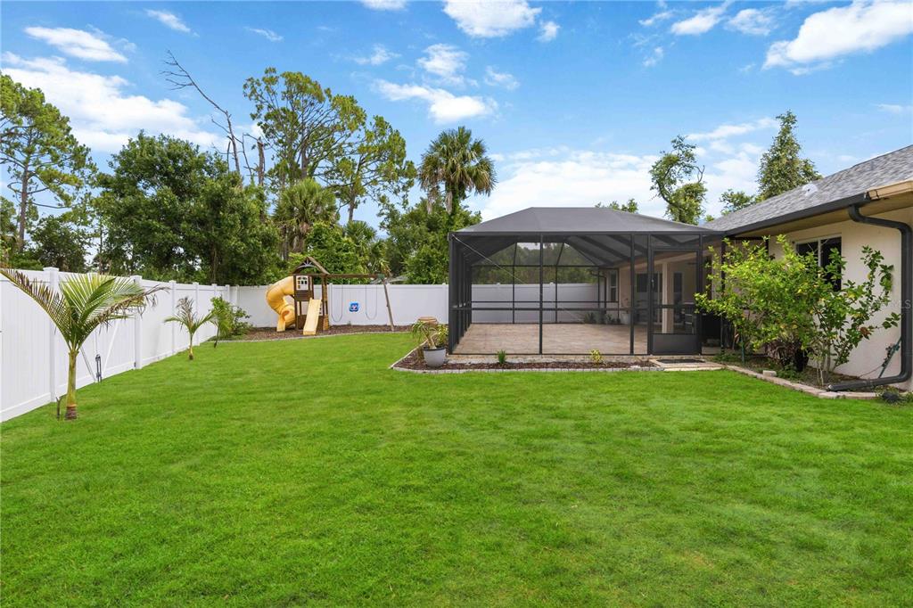 A backyard features a screened-in patio, a grassy lawn, a white fence, and a playset — 3691 SESAME STREET, NORTH PORT, FL