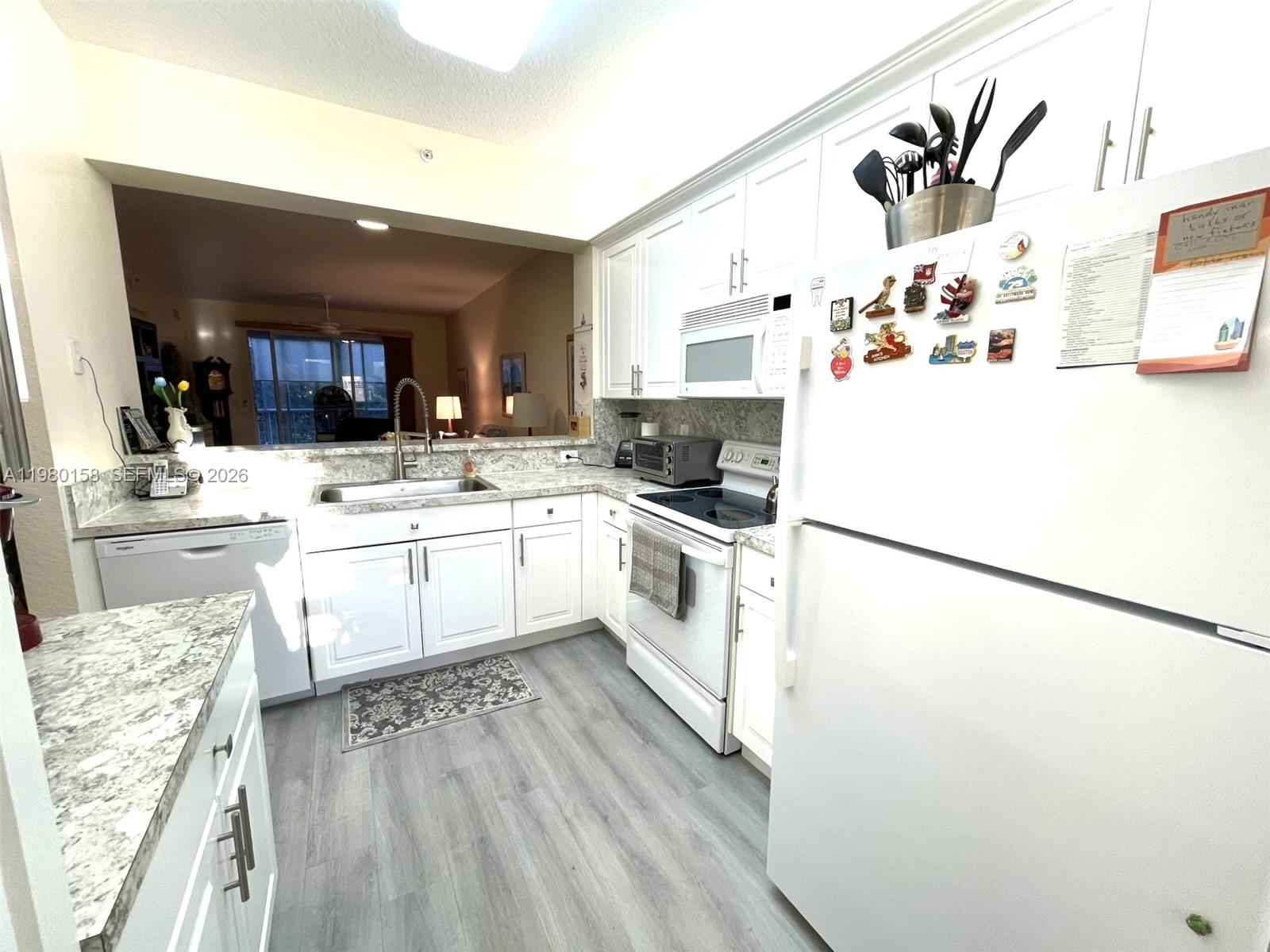 A white kitchen features gray-veined countertops, stainless steel appliances, and light wood-look flooring — 7775 Yardley Dr # 409, Tamarac FL 33321, TAMARAC, FL