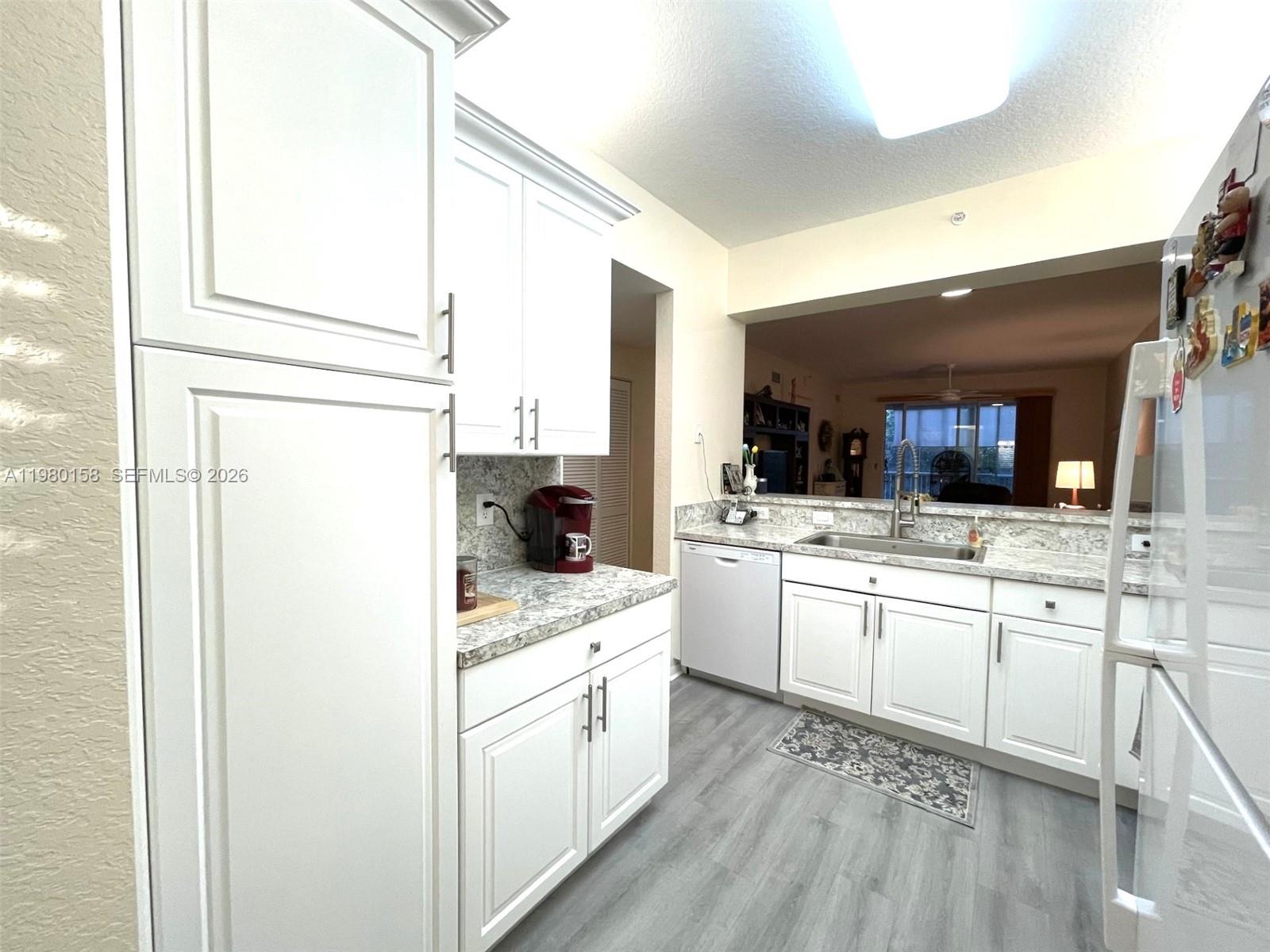 A kitchen features white cabinets, granite countertops, stainless steel sink, and light gray flooring — 7775 Yardley Dr # 409, Tamarac FL 33321, TAMARAC, FL