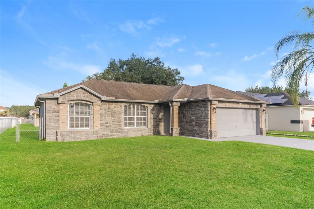 A single-story house with a stone facade, a two-car garage, and a green lawn — 611 BASINGSTOKE COURT, KISSIMMEE, FL