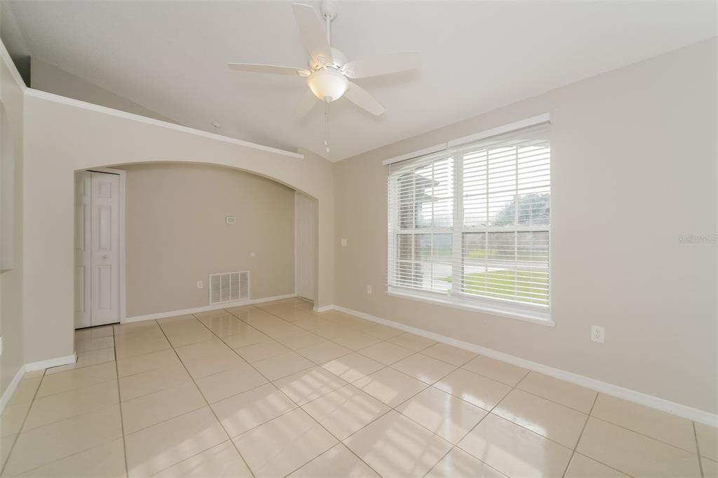 An empty room with beige tile flooring, a ceiling fan, and a large window — 611 BASINGSTOKE COURT, KISSIMMEE, FL