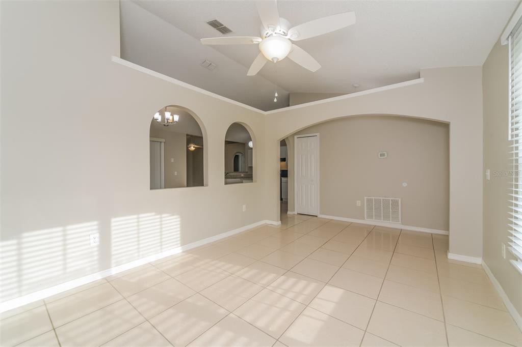A bright, tiled living room features vaulted ceilings, a ceiling fan, and arched wall cutouts — 611 BASINGSTOKE COURT, KISSIMMEE, FL
