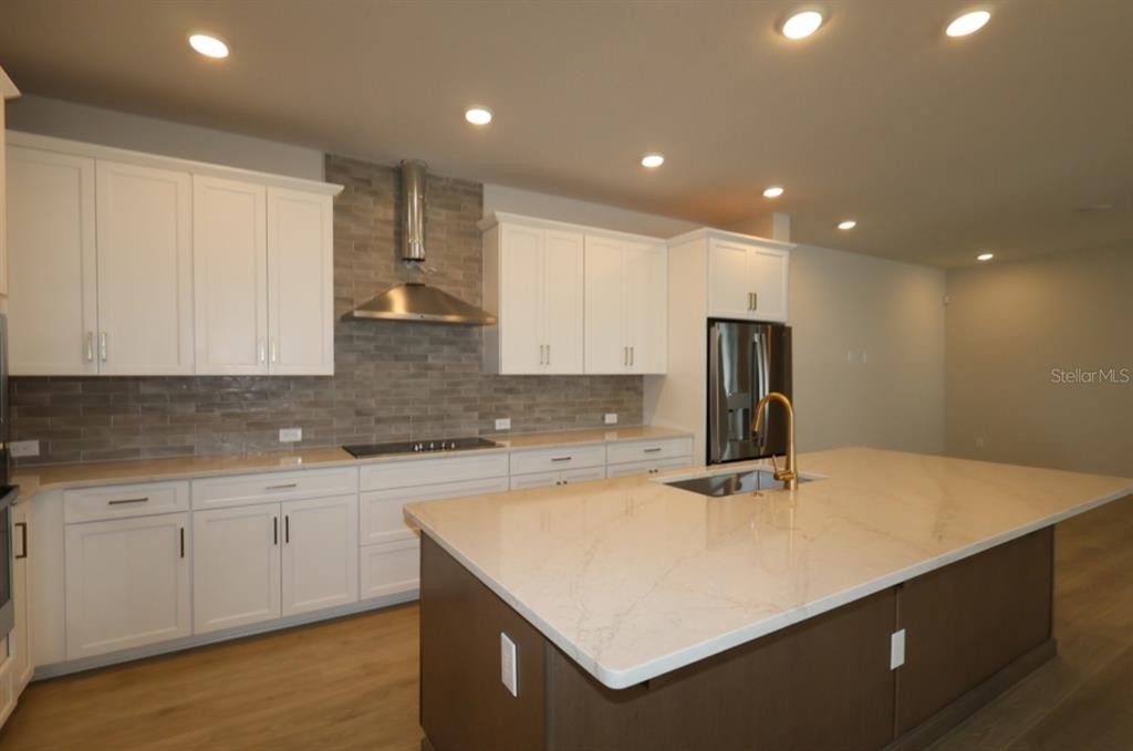 A modern kitchen features white cabinets, a large island, stainless steel appliances, and tile backsplash — 14975 SIRLEAF DRIVE, ORLANDO, FL