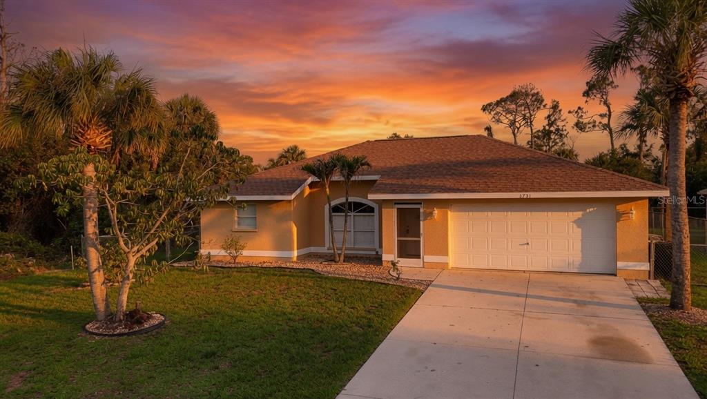 A single-story house with a tan exterior, a two-car garage, and palm trees at sunset — 3781 WAYWARD AVENUE, NORTH PORT, FL