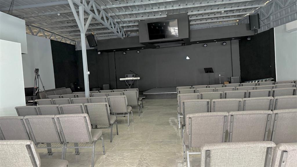 An indoor assembly hall features rows of gray chairs facing a stage with a screen — 156 SECTOR, KM 13.5 PR-156, BARRANQUITAS, PR
