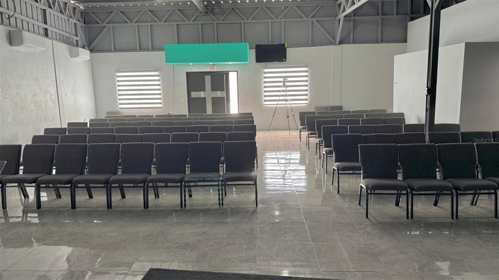 A large, open room with rows of black chairs, tiled floors, and a metal ceiling — 156 SECTOR, KM 13.5 PR-156, BARRANQUITAS, PR