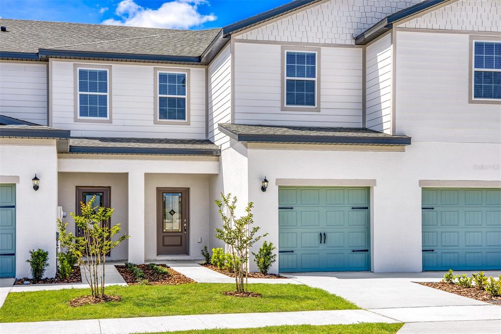 The exterior of a two-story townhouse features white siding, a brown front door, and blue garage doors — 721 POPPY LANE, DUNDEE, FL