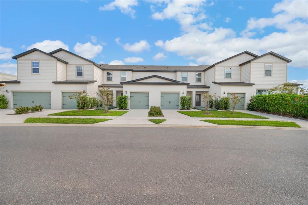A row of four attached townhomes with light siding, green garage doors, and landscaped front yards — 721 POPPY LANE, DUNDEE, FL