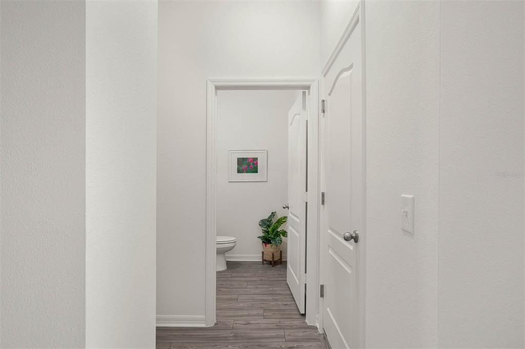 A hallway with wood-look flooring leads to a bathroom featuring a toilet and a plant — 721 POPPY LANE, DUNDEE, FL