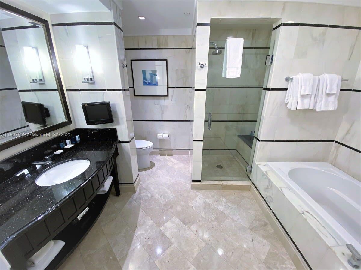 A bathroom features a black vanity, a glass-enclosed shower, and a white soaking tub — 4391 Collins Ave # 1619, Miami Beach FL 33140, MIAMI BEACH, FL