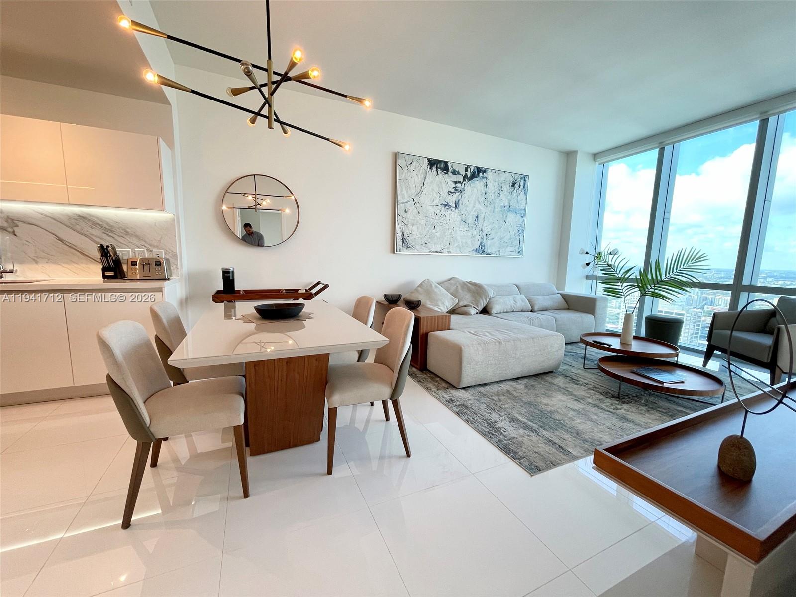 A modern open-concept living and dining area features white tile floors and floor-to-ceiling windows — 851 NE 1st Ave # 3606, Miami FL 33132, MIAMI, FL
