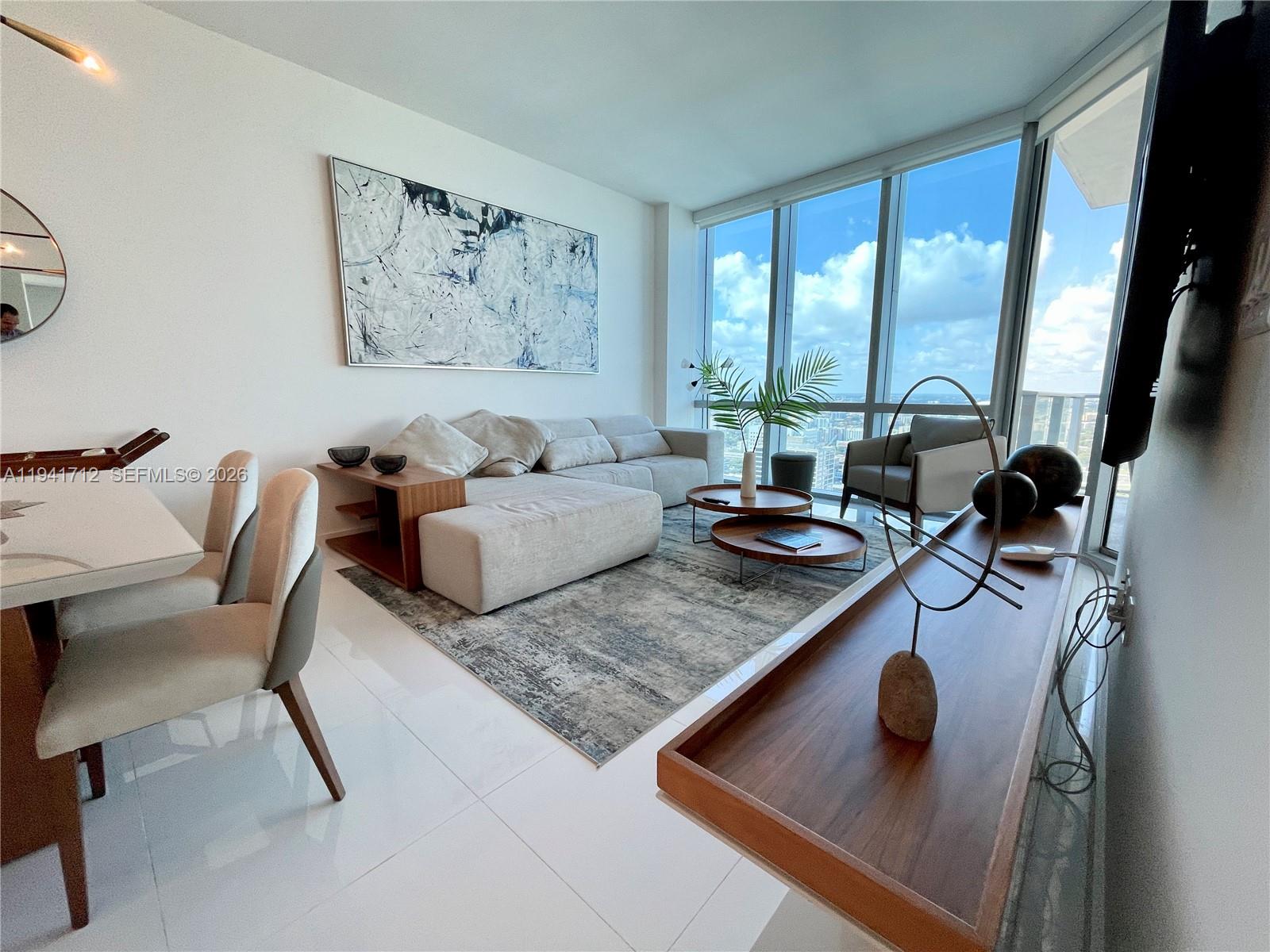 A modern living room features a sectional sofa, dining area, and floor-to-ceiling windows — 851 NE 1st Ave # 3606, Miami FL 33132, MIAMI, FL
