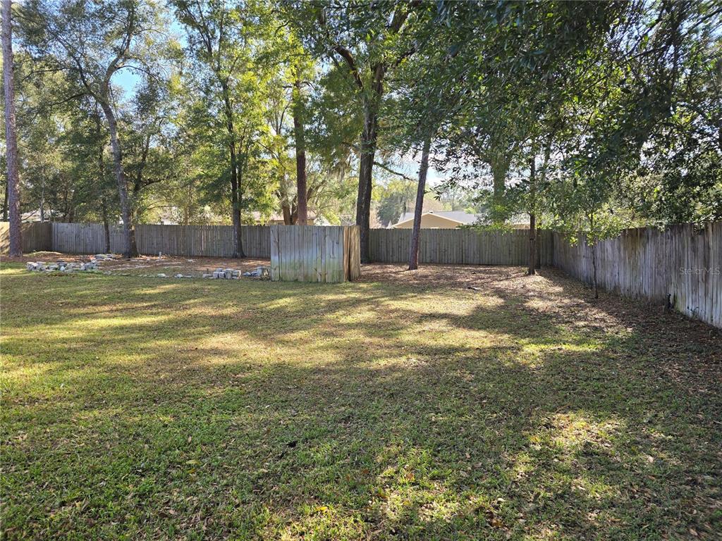 A grassy backyard features a wooden fence, mature trees, and a small wooden shed — 5904 SW 107TH STREET, OCALA, FL