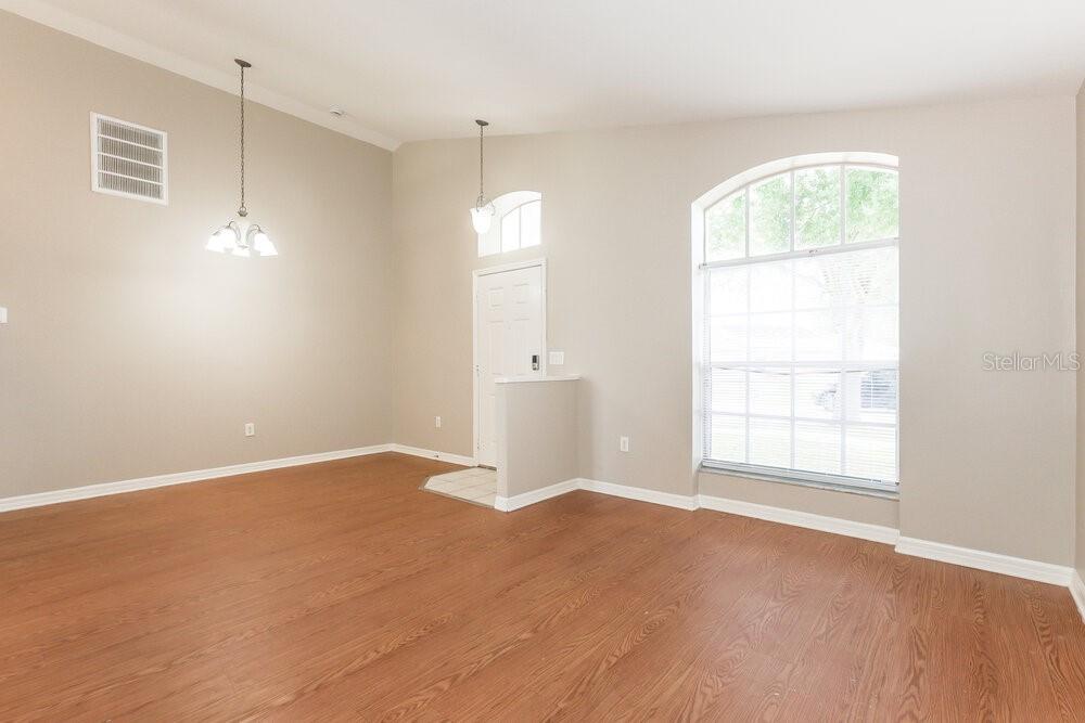 An empty room with light-colored walls, wood-look flooring, a large arched window, and pendant lighting — 11109 LAKE LANIER DRIVE, RIVERVIEW, FL