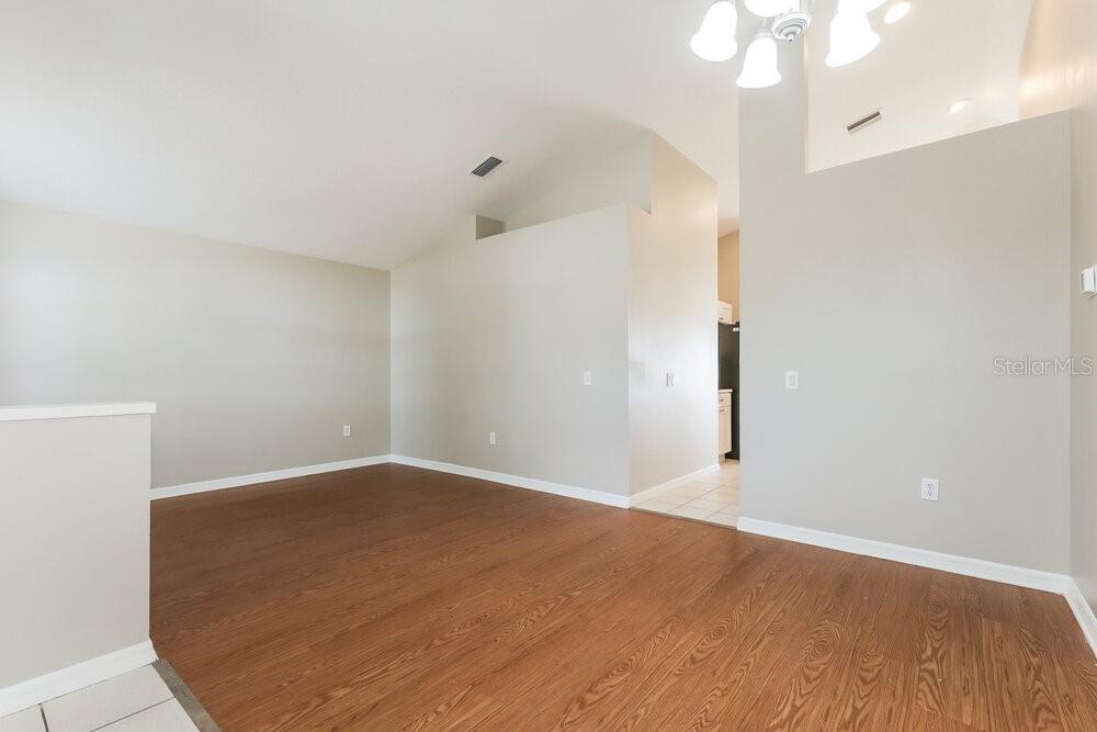 An empty room with vaulted ceilings, wood-look flooring, and a light fixture — 11109 LAKE LANIER DRIVE, RIVERVIEW, FL