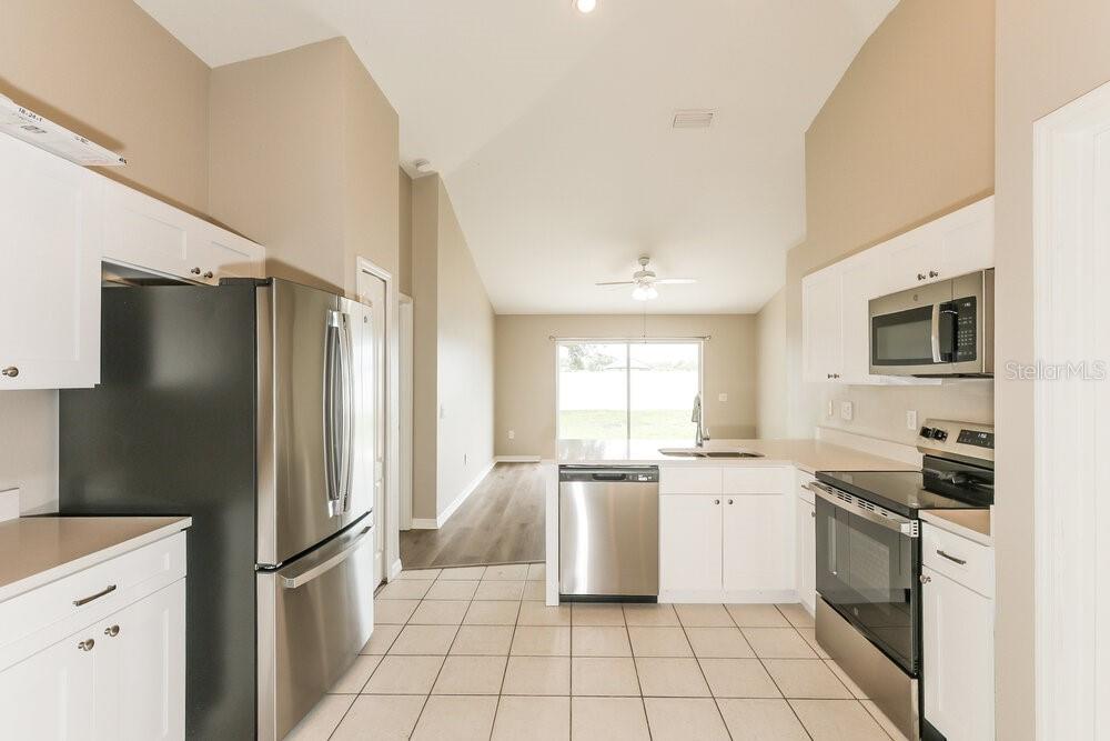 A kitchen with white cabinets, stainless steel appliances, and tile flooring opens to a living area — 11109 LAKE LANIER DRIVE, RIVERVIEW, FL