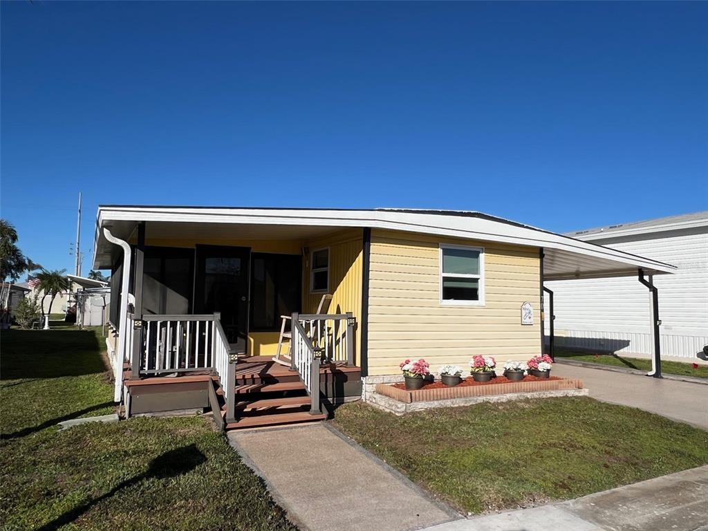 A yellow mobile home features a front porch, a carport, and a small flower bed — 11300 124TH AVENUE UNIT 70, LARGO, FL