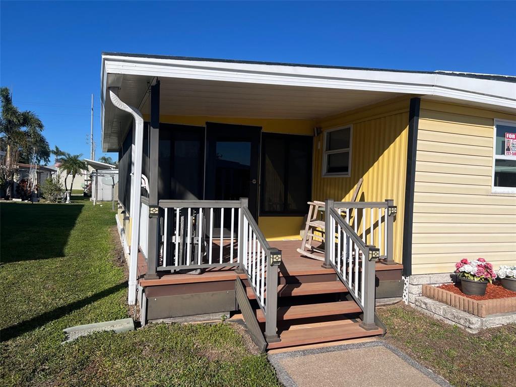 A yellow mobile home features a covered front porch with wooden stairs and railings — 11300 124TH AVENUE UNIT 70, LARGO, FL