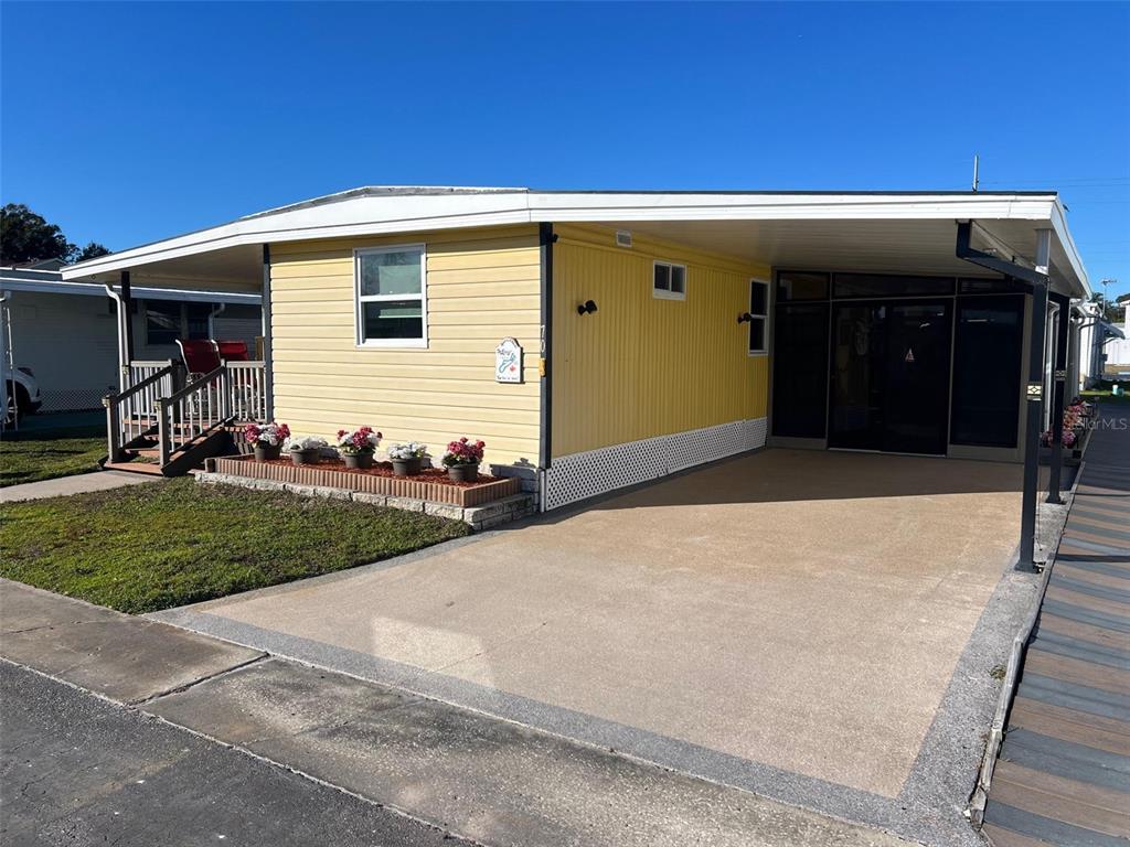 A yellow mobile home features a concrete driveway, a carport, and a small front garden — 11300 124TH AVENUE UNIT 70, LARGO, FL