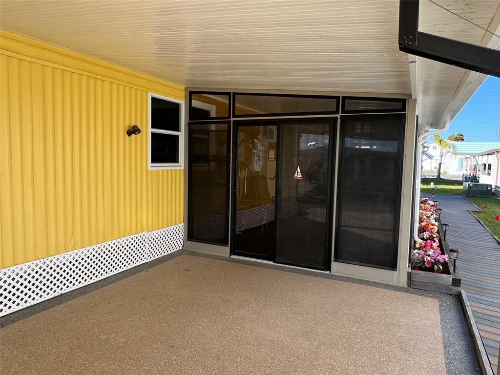 A covered patio with a yellow corrugated wall, sliding glass doors, and a concrete floor — 11300 124TH AVENUE UNIT 70, LARGO, FL