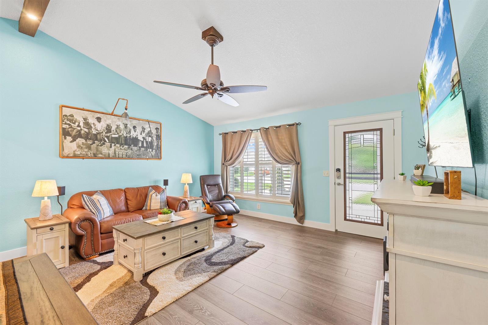 A living room features light blue walls, a brown leather sofa, and wood-look flooring — 128 Banyan Circle, Jupiter FL 33458, JUPITER, FL