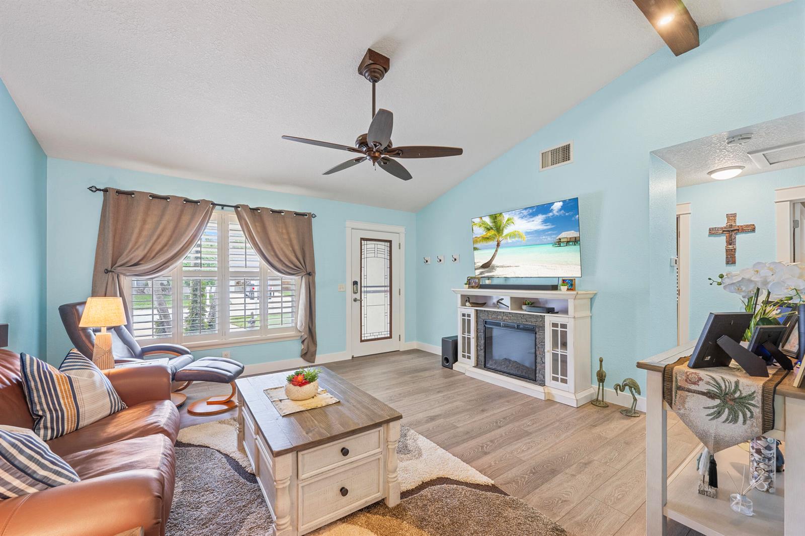 A living room features light blue walls, wood-look flooring, a fireplace, and a ceiling fan — 128 Banyan Circle, Jupiter FL 33458, JUPITER, FL