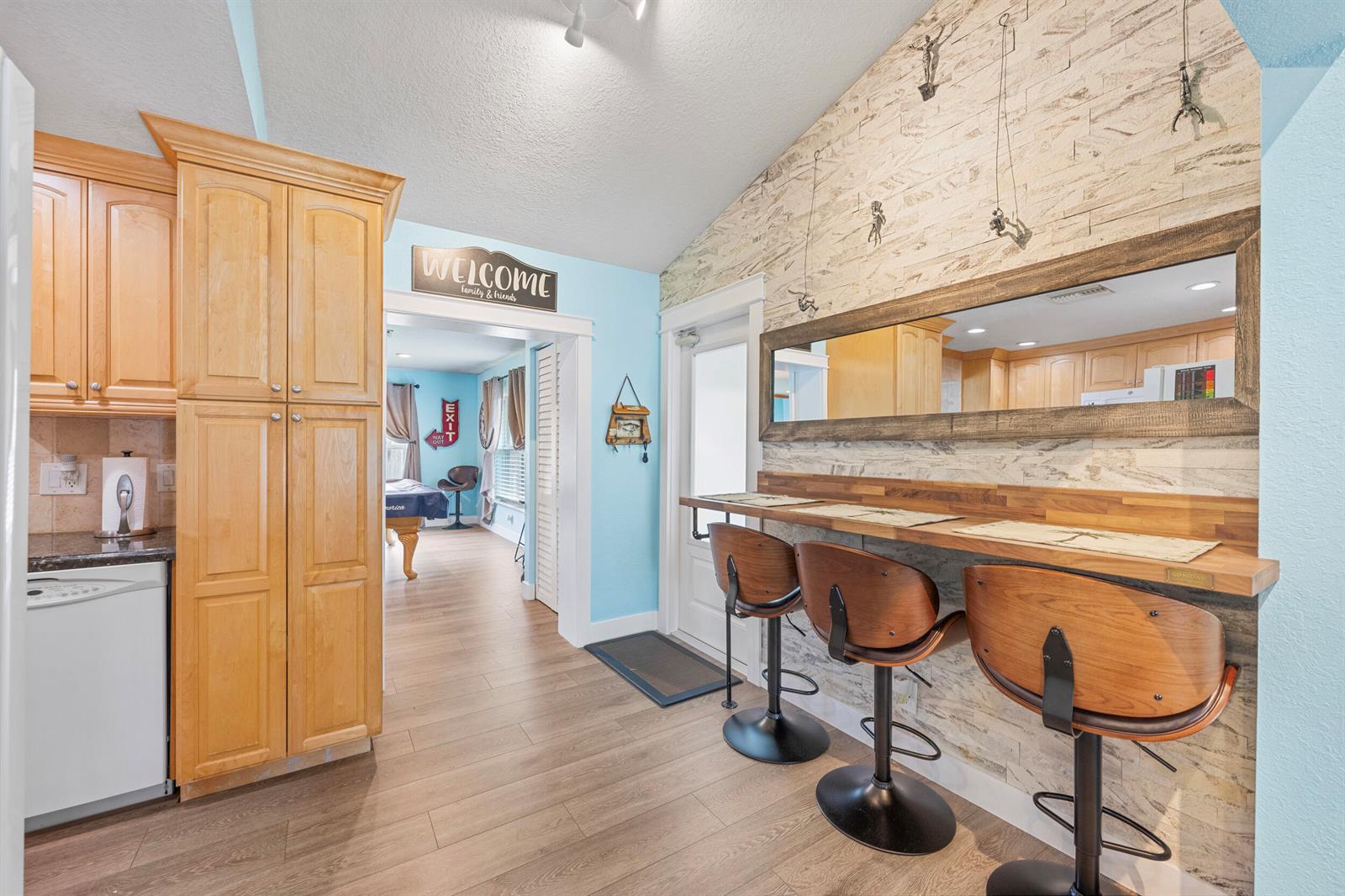 A kitchen area features a wooden bar with three stools, light blue walls, and a mirror — 128 Banyan Circle, Jupiter FL 33458, JUPITER, FL
