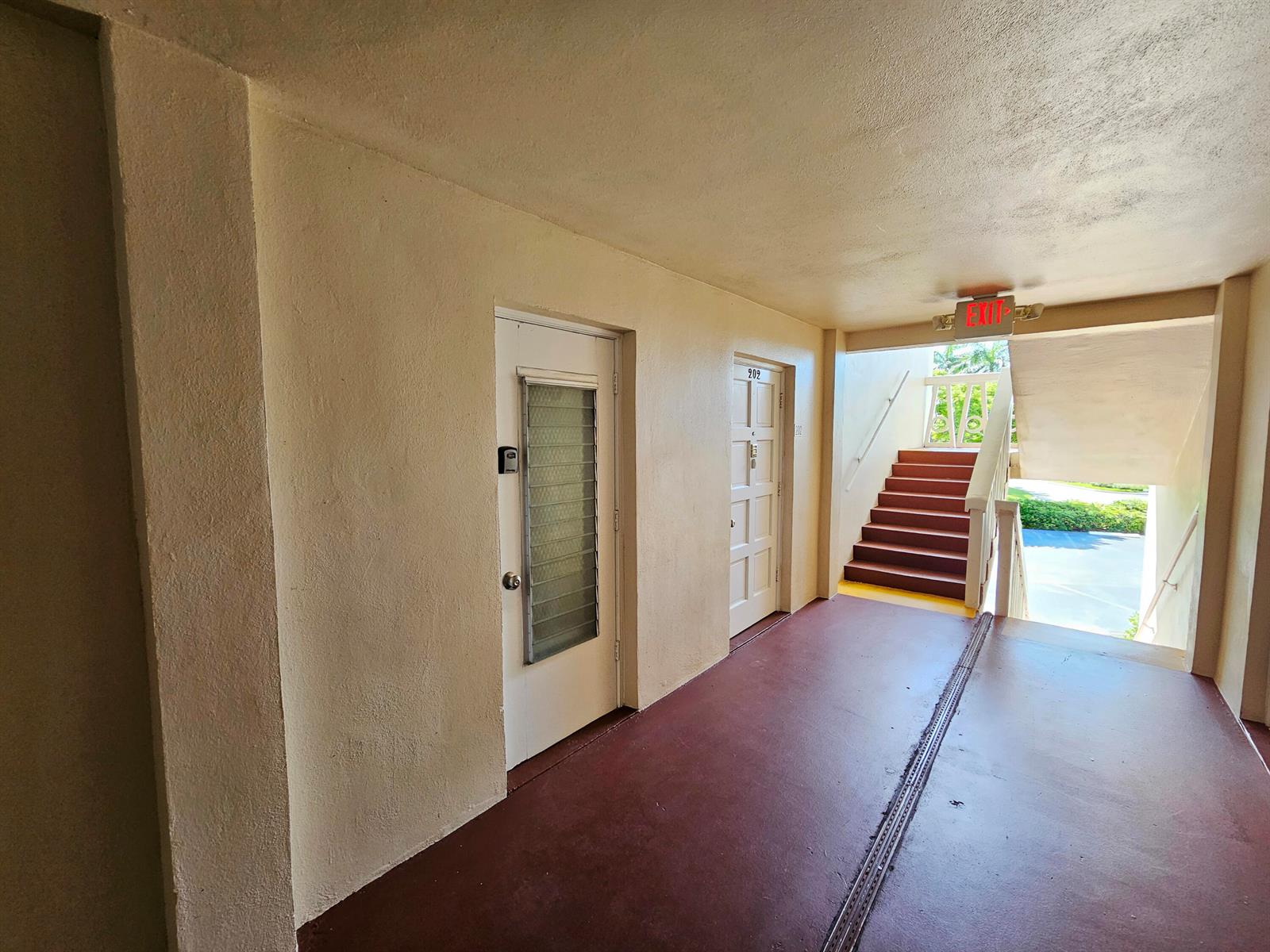 An outdoor apartment hallway features two white doors, a red floor, and a staircase — 2562 Garden Drive N # 202, FL 33461, FL