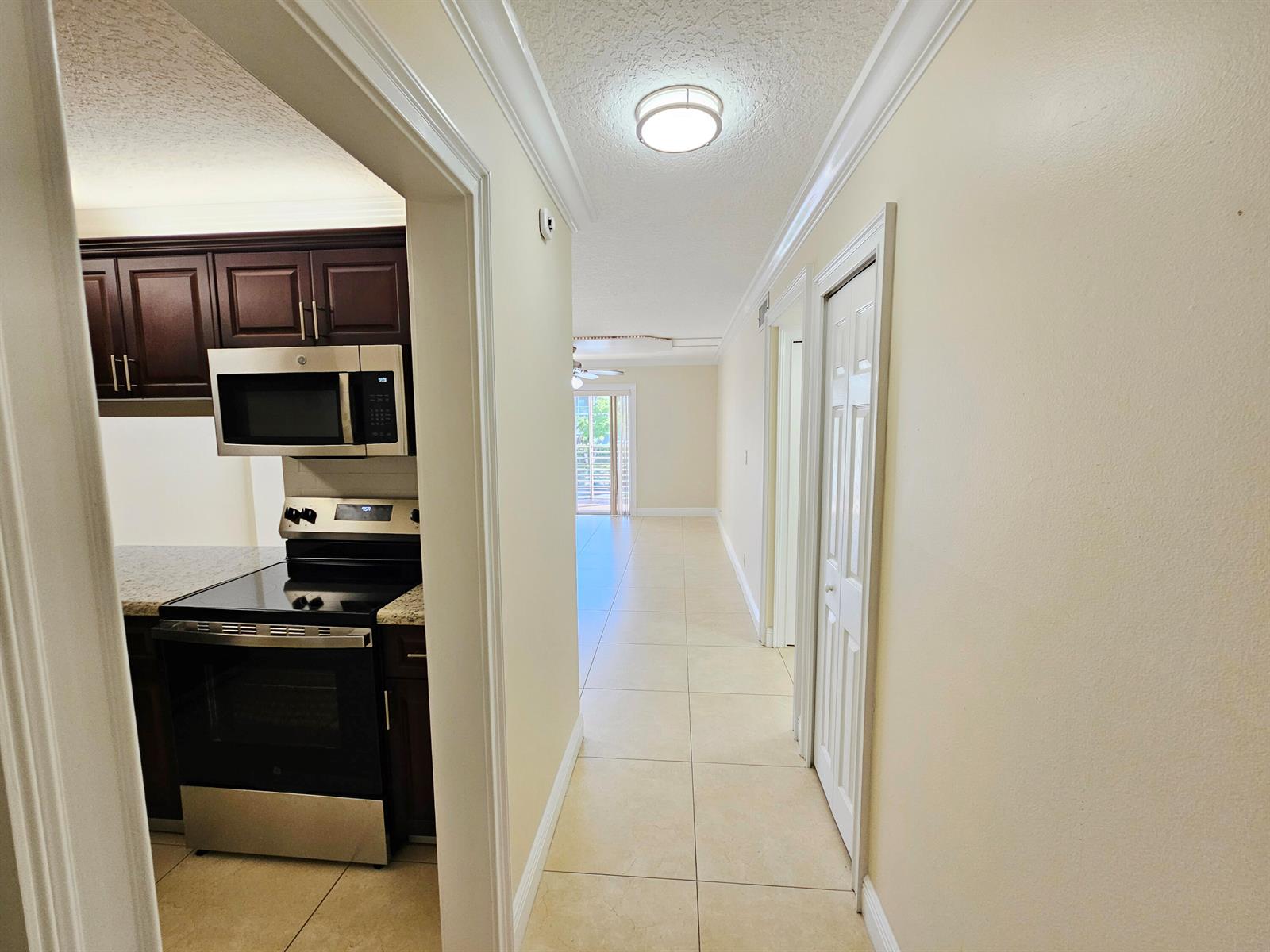 A hallway with tile floors leads past a kitchen with dark cabinets to a balcony — 2562 Garden Drive N # 202, FL 33461, FL