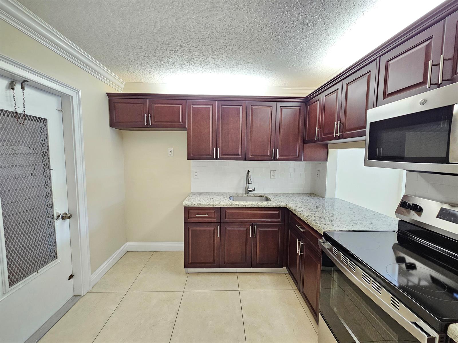 A kitchen features dark wood cabinets, granite countertops, a stainless steel sink, and stainless appliances — 2562 Garden Drive N # 202, FL 33461, FL