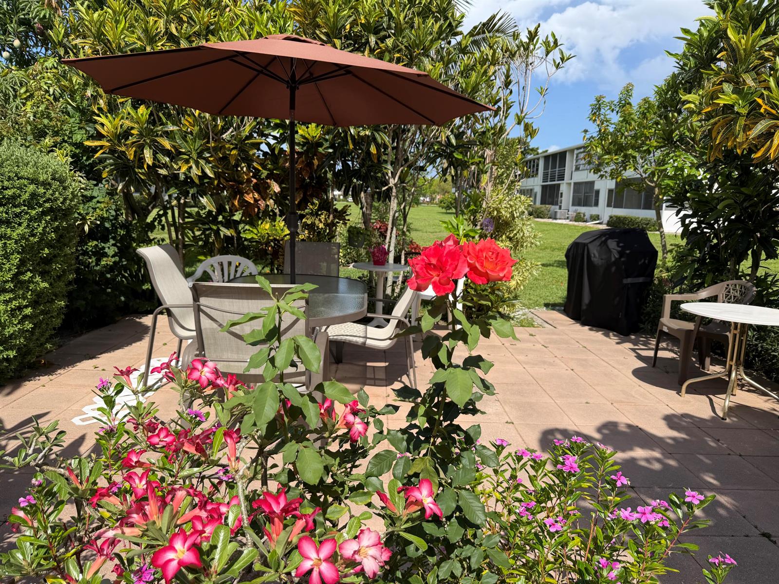 A patio features a dining set with a brown umbrella, rose bushes, and potted plants — 162 Windsor H, West Palm Beach FL 33417, WEST PALM BEACH, FL