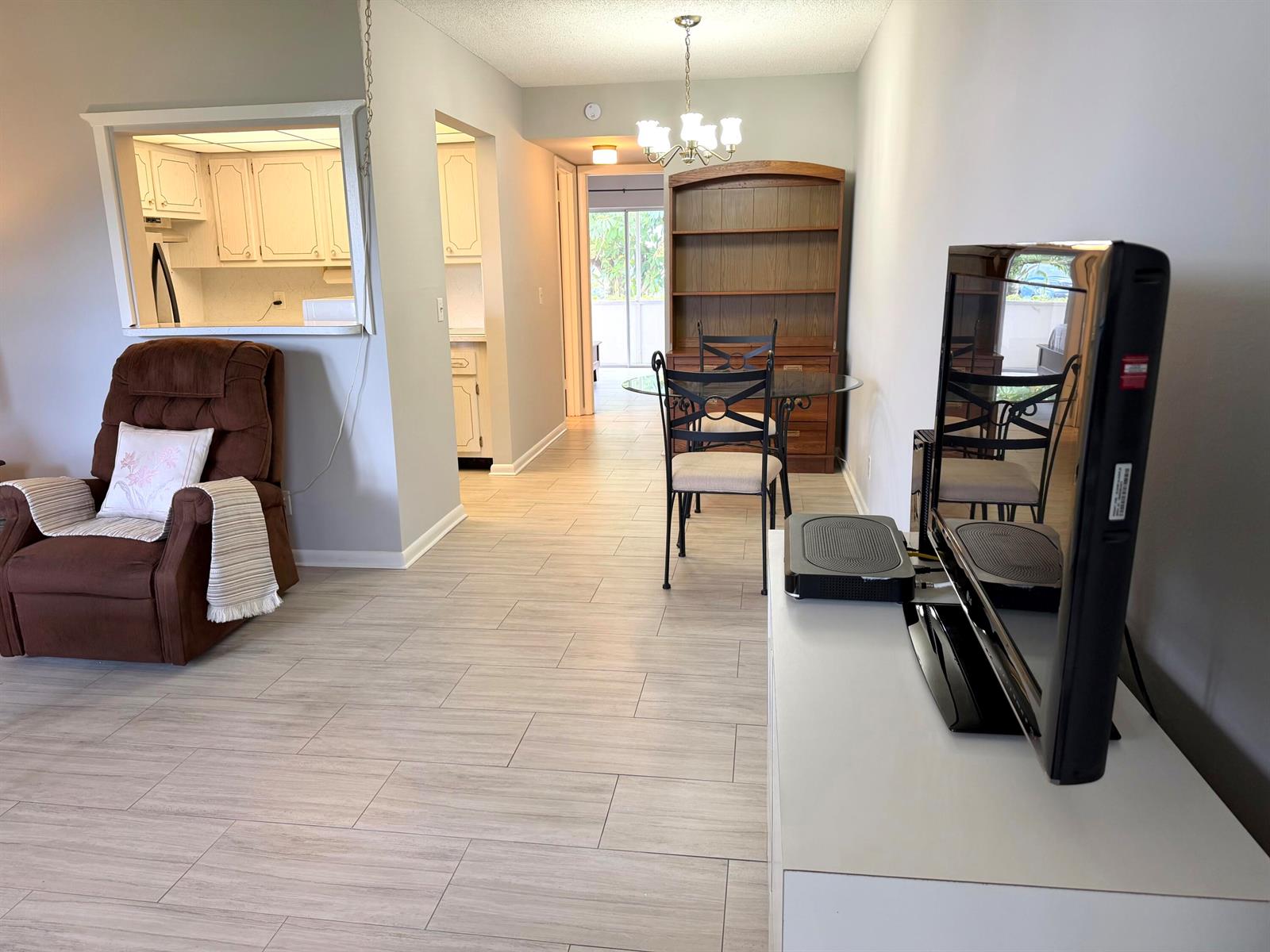 A living room and dining area feature light wood-look tile flooring and a pass-through kitchen — 162 Windsor H, West Palm Beach FL 33417, WEST PALM BEACH, FL