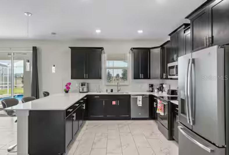 A modern kitchen features dark cabinetry, white countertops, stainless steel appliances, and tile flooring — 913 OCEAN COURSE AVENUE, DAVENPORT, FL