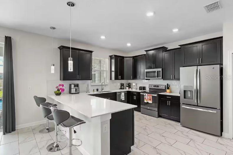 A kitchen with dark cabinets, stainless steel appliances, a white island, and light tile flooring — 913 OCEAN COURSE AVENUE, DAVENPORT, FL