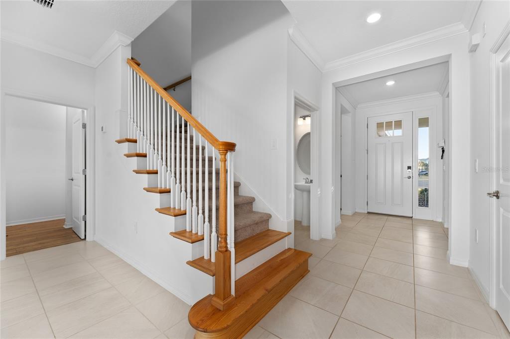 A bright entryway features a carpeted staircase with a wooden handrail and light tile flooring — 2834 HIGH POINTE STREET, CLERMONT, FL