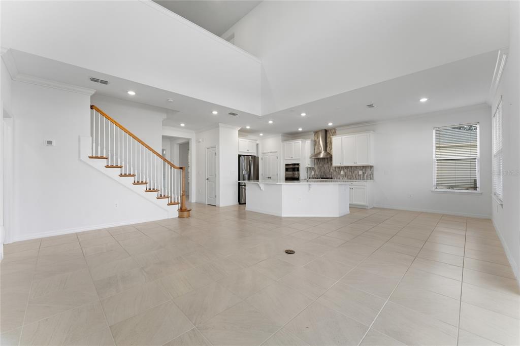 A spacious open-concept kitchen and living area with white cabinets, tile flooring, and a staircase — 2834 HIGH POINTE STREET, CLERMONT, FL