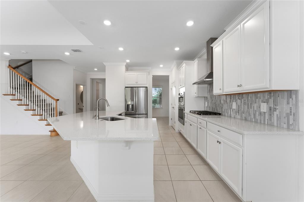 A modern kitchen features white cabinets, a large quartz island, and a staircase nearby — 2834 HIGH POINTE STREET, CLERMONT, FL