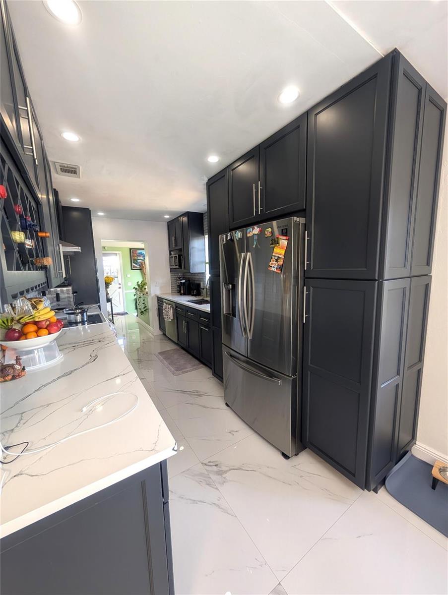 A kitchen features dark cabinetry, stainless steel appliances, and white marble-patterned countertops and flooring — 1313 NW 58th Avenue, Margate FL 33063, MARGATE, FL