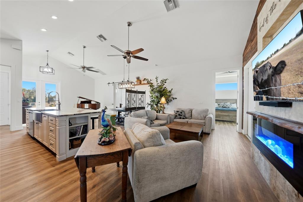 A living room and kitchen area with light wood floors, a fireplace, and vaulted ceilings — 9931 SE ENGLISH AVENUE, ARCADIA, FL