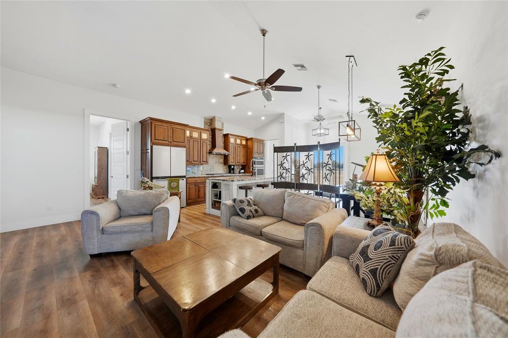 An open-concept living room and kitchen featuring wood-look flooring, neutral furniture, and wooden cabinetry — 9931 SE ENGLISH AVENUE, ARCADIA, FL