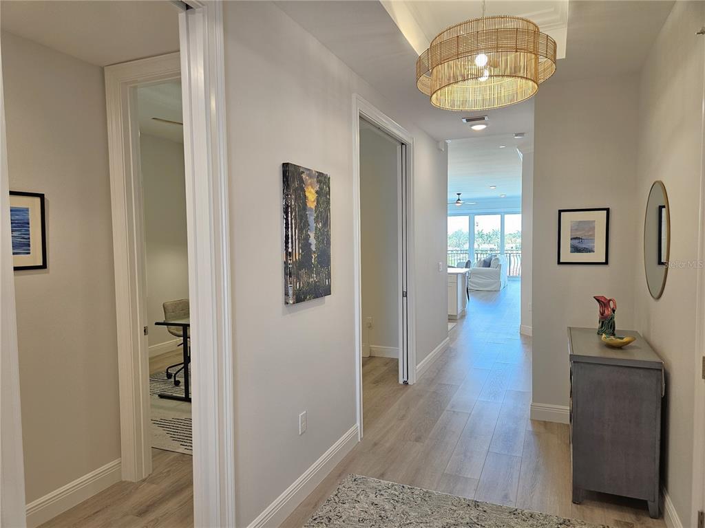 A hallway with light wood floors leads to an open living area with a chandelier — 503 TAMIAMI TRAIL N UNIT 301, VENICE, FL